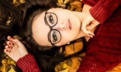 a woman with glasses laying on a bed of leaves