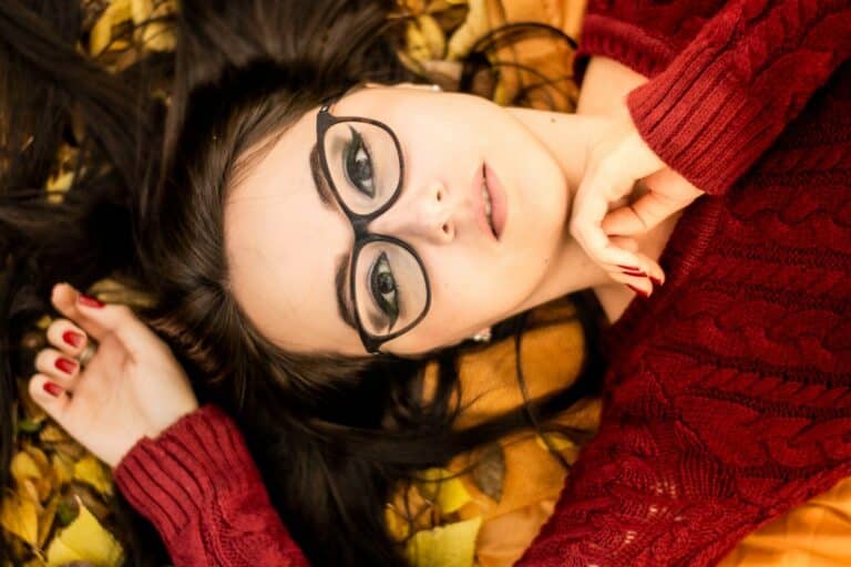 a woman with glasses laying on a bed of leaves