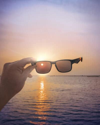 Eine Hand hält eine Sonnenbrille im Hintergrund ist das Meer zu sehen 